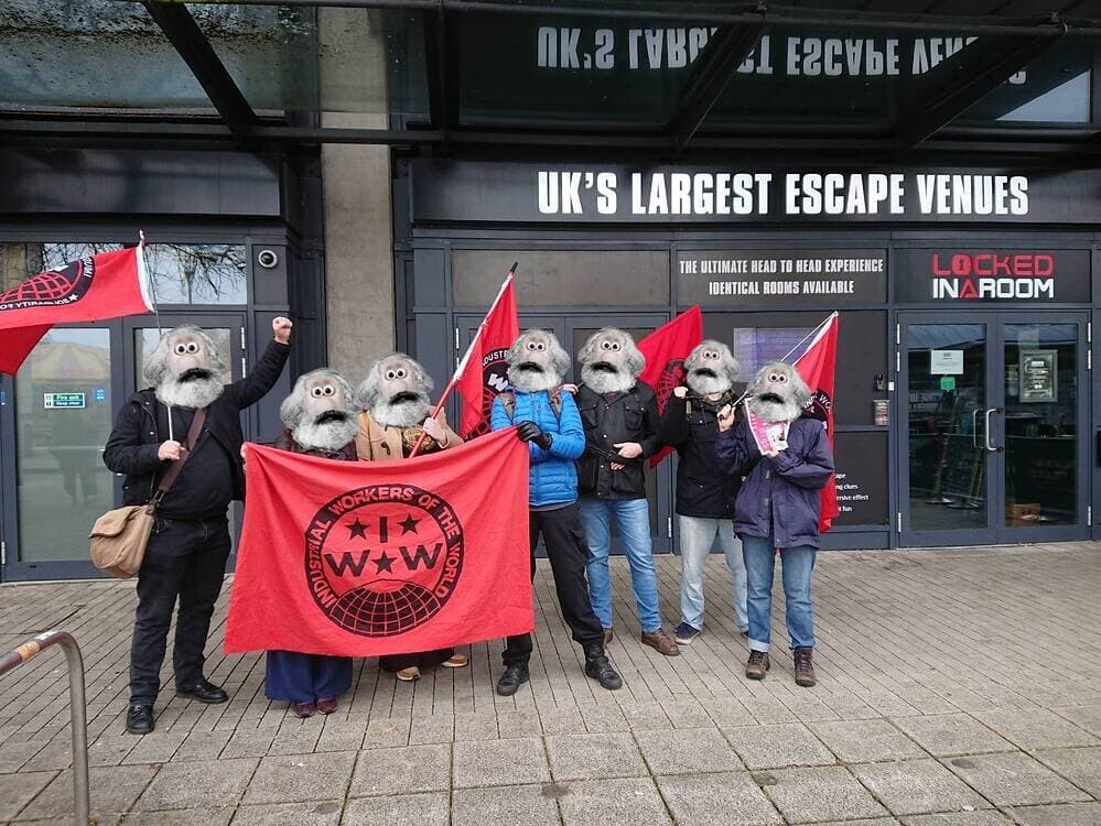 picture shows group of union members (faces covered by Wallace and Gromit Faces) demonstrating outside of workplace